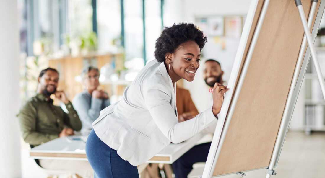 Creative black woman, meeting and writing on Flipchart for team building, coaching or activity at office. Happy African American female in presentation using board to write idea or FAQ for startup